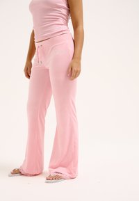 Lichtroze loungewear set met een aansluitend tanktop en flared broek met een trekkoord in de taille, textuurstof en kantaccenten bij de manchetten.