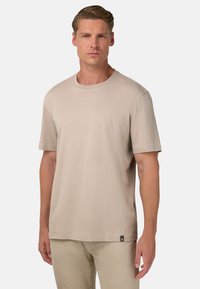 Béžové tričko s krátkym rukávom vyrobené z mäkkej bavlny, s okrúhlym výstrihom. Obsahuje malú značkovú nášivku na dolnom leme.