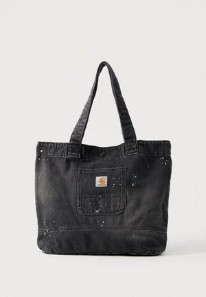 Sac cabas en toile noire avec anses réglables, poche avant et détails de projections de peinture blanche sur fond uni.