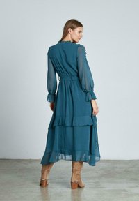 Teal, schichtkleid bis zum Boden mit transparenten Ärmeln, Rüschenausschnitt und Taillenband. Es zeichnet sich durch ein fließendes Design mit strukturiertem Finish aus.