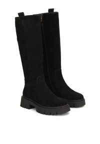 Botas altas de ante negro hasta la rodilla con suela plana y gruesa, cremallera lateral y dos tiradores en la parte superior para facilitar su ajuste. Textura suave sin patrones visibles.