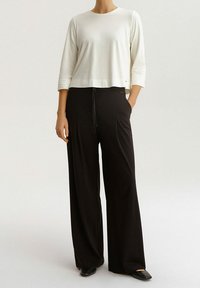 Top bianco a tre quarti abbinato a pantaloni neri a gamba larga. I pantaloni hanno una vita con coulisse, creando un silhouette rilassata.