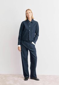 Ensemble veste et pantalon en denim bleu foncé à rayures verticales, avec un col à revers, des boutons comme fermeture, et des poches latérales.