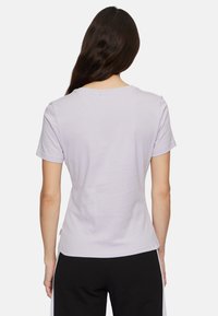 Camiseta de color púrpura claro con mangas cortas, escote redondo y una textura de algodón suave. Presenta una etiqueta en la costura izquierda.