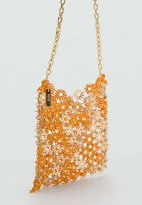 Oranje schoudertas met bloemenpatroon, gemaakt van glanzend plastic materiaal, voorzien van een gouden kettingband en een klein metalen logo label.
