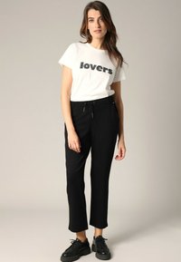 Witte T-shirt met zwarte tekst "lovers", gecombineerd met zwarte cropped broek en zwarte sneakers. Eenvoudig ontwerp, katoenen materiaal, relaxte pasvorm.