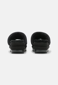 Czarne buty wsuwane z miękkim, puszystym wnętrzem i grubymi, amortyzowanymi podeszwami. Projekt ma zaokrąglony kształt, gładką teksturę i minimalne akcenty.