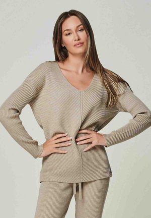 Beige gerippter Strickpullover mit V-Ausschnitt, langen Ärmeln und einer lockeren Passform. Mit einem verdrehten Detail an der Vorderseite und strukturiertem Stoff.