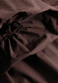 Σκούρο καφέ ύφασμα με ορατές ρυτίδες και συγκεντρωμένη ελαστική λεπτομέρεια, δημιουργώντας υφασμάτινες πτυχώσεις και σκιάσεις.