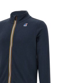 Giacca navy con zip e colletto alto, presenta strisce multicolori lungo la cerniera e una toppa con logo sul lato sinistro del petto. Tessuto morbido e strutturato.