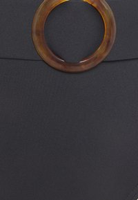 Schwarzer Stoff mit glatter Textur, versehen mit einem großen runden Akzent aus Schildpatt an der Taille. Schlichtes, geradliniges Design.