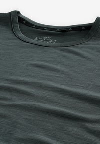 Camisa de ropa deportiva en gris oscuro, hecha de una tela suave y texturizada. Cuenta con un cuello redondo y un sutil logo cerca del cuello.