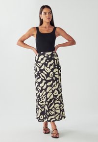 Czarny top na ramiączkach w połączeniu z długą, wzorzystą spódnicą z kremowymi abstrakcyjnymi wzorami. Gładka tkanina o płynnym kroju. Proste sandały.