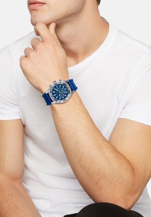 Blå silikonerem watch med et sølv metal hus, blå urskive og chronograph funktioner. Store markeringer og forskellige teksturer forbedrer synligheden.