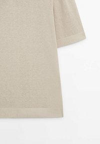 Pull en maille beige à manches courtes avec poignets et ourlet côtelés, présenté sur fond blanc.