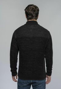 Schwarzer Strickpullover mit geripptem Kragen und Bündchen, strukturierter Stoff in unterschiedlichen Farbtönen, Rückansicht, kombiniert mit blauen Jeans.