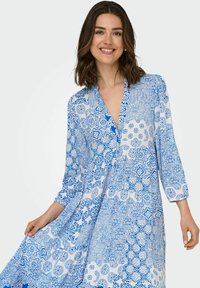 Vestito a strisce blu e bianche con scollatura a V, maniche a tre quarti e tessuto fluido che mette in mostra disegni e forme intricate.