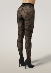 Collant neri a fantasia floreale, con una texture trasparente, vita alta e abbinati a scarpe nere con tacco alto.