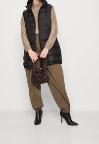 Svart puffer-väst med hög krage, brun stickad tröja, olivgröna byxor och en liten brun satinhandske. Spetsiga svarta klackar.