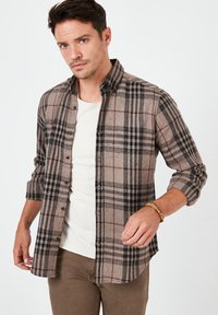 Bruin en zwart geruit flanellen shirt met knoopsluiting, lange mouwen en een zachte textuur, gedragen over een wit T-shirt.