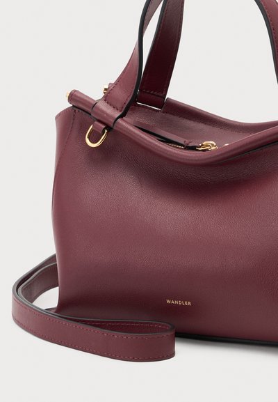 Sac à main en cuir rouge foncé avec poignées courtes, bandoulière amovible, détails dorés et petit logo doré près du centre en bas.