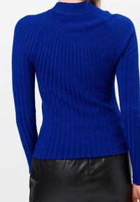 Niebieski prążkowany sweter z długimi rękawami i wysokim kołnierzem, wykonany z teksturowanej tkaniny o dopasowanym kroju, zestawiony z czarną skórzaną spódnicą.