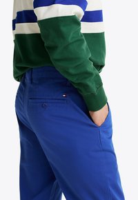 Niebieskie bawełniane spodnie w slim fit, z bocznymi i tylnymi kieszeniami oraz akcentem logo na tylnej kieszeni, połączone z zielono-białym swetrem w paski.