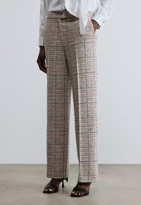 Checkered plaid trousers in beige, pink, and gray blend; wide-leg design; textured fabric; paired with black heeled sandals.