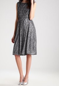 Svart och silver knälång klänning med veck, ärmlös design, texturerad tyg, kombinerad med blanka silverklackar.