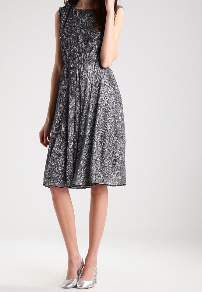 Svart och silver knälång klänning med veck, ärmlös design, texturerad tyg, kombinerad med blanka silverklackar.