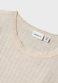 Svijetložuta košulja s teksturiranim uzorkom, s izrezom od čipke u obliku školjke i oznakom na tkanini koja sadrži informacije o veličini.