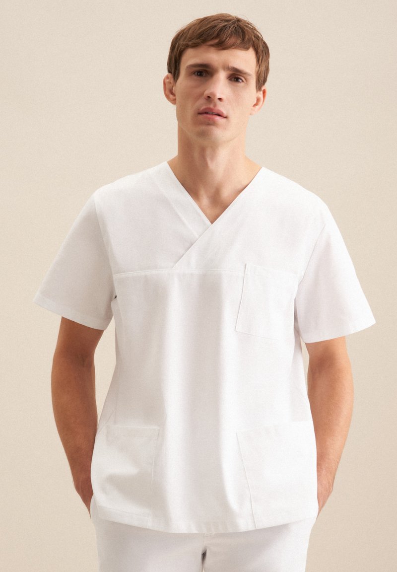 Tunique médicale blanche avec un col en V, des manches courtes et une poche avant. Le matériau semble lisse et respirant, adapté aux environnements de santé.