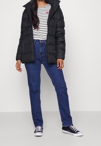 Musta toppatakki vetoketjulla edessä, päällä valkoinen raidallinen paita, jossa pieni vaaleanpunainen sydän. Siniset suoralahkeiset farkut ja mustat lenkkarit.