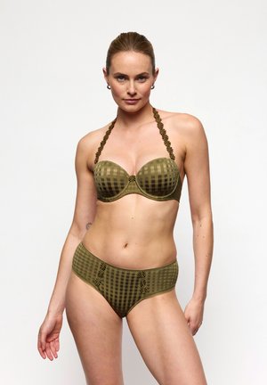 Frau trägt olivgrünes kariertes Bikini mit floralen Trägerdetails, steht vor weißem Hintergrund, schaut nach vorne.