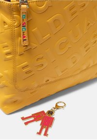 Yellow nylon tote bag with embossed logo, featuring a colorful keychain of two stylized figures in red and gold hardware.
