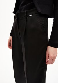 Black tailored trousers with a slim fit, featuring a flat front, side pockets, and a subtle brand tag on the waistband.