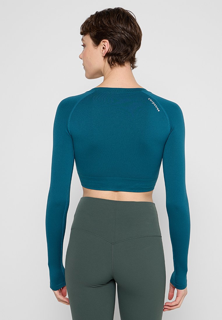 Türkiser langärmliger Crop-Top mit rundem Ausschnitt und Daumenlöchern, aus strukturiertem Stoff und kleinem Logo im oberen Rückenbereich.