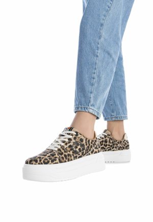 Sneaker con stampa leopardata, suola bianca, punta tonda e lacci piatti, abbinate a pantaloni di denim azzurri chiari con risvolto.