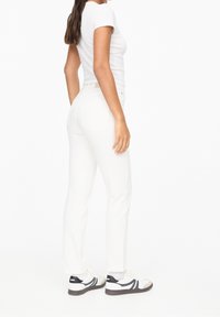 Jeans de mezclilla blanca con un diseño de pierna recta, que presentan una textura suave y un estilo de cinco bolsillos. Combinados con una camiseta blanca y zapatillas.