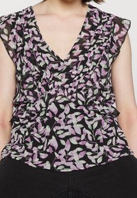 Haut à fleurs en tissu léger avec un fond noir et des feuilles violettes et vertes. Il présente un décolleté en V profond et des détails volantés.