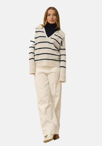 Randig pullovertröja i kräm och marinblå, med V-ringning, långa ärmar och oversized passform; kombinerad med krämvita vida byxor.
