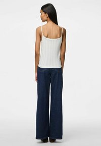 Top de punto crema sin mangas con tirantes estrechos, combinado con unos jeans de mezclilla oscuros de pierna ancha y cintura alta. La tela tiene una sutil textura y detalle de canalé.