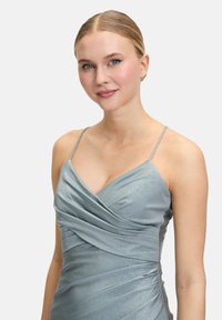 Robe de soirée bleu clair en satin avec des fines bretelles. Présente un buste drapé et une texture brillante, avec des fronces sur les côtés.