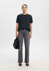 Juoda marškinėliai su apvalia iškirpte, pilkos aukšto liemens džinsai, juodos smailios aukštakulnės, juoda struktūruota rankinė su rankena ir priekinėmis detalėmis.