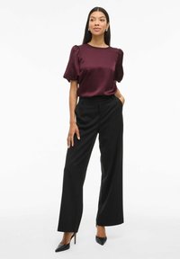 Top in satin bordeaux con maniche a sbuffo, abbinato a pantaloni a gamba larga neri a vita alta e décolleté neri a punta. Accenti di gioielli semplici.