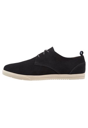 Zwarte suède veterschoenen voor dagelijks gebruik met een witte rubberen zool en een kleine stoffen lus bij de hiel.