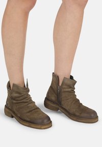 Bottines en cuir marron avec un design décontracté, fermeture éclair latérale, bout rond et talon en bois empilé. Texture douce et finition mate.