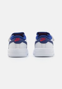 White Nike sneakers with blue accents, featuring a textured design, padded collar, and red Nike logo on the heel and tongue.