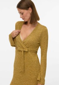 Garās piedurknes apvilkta kleita sinepju dzeltenā ribota auduma ar dziļu V veida kakla izgriezumu un sasietu jostasvietu, lai izveidotu pieguļošu siluetu.