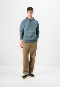 Sudadera de rayas color azul claro con un bolsillo frontal, combinada con pantalones de pierna ancha color beige y zapatillas negras con cordones blancos y suela marrón.